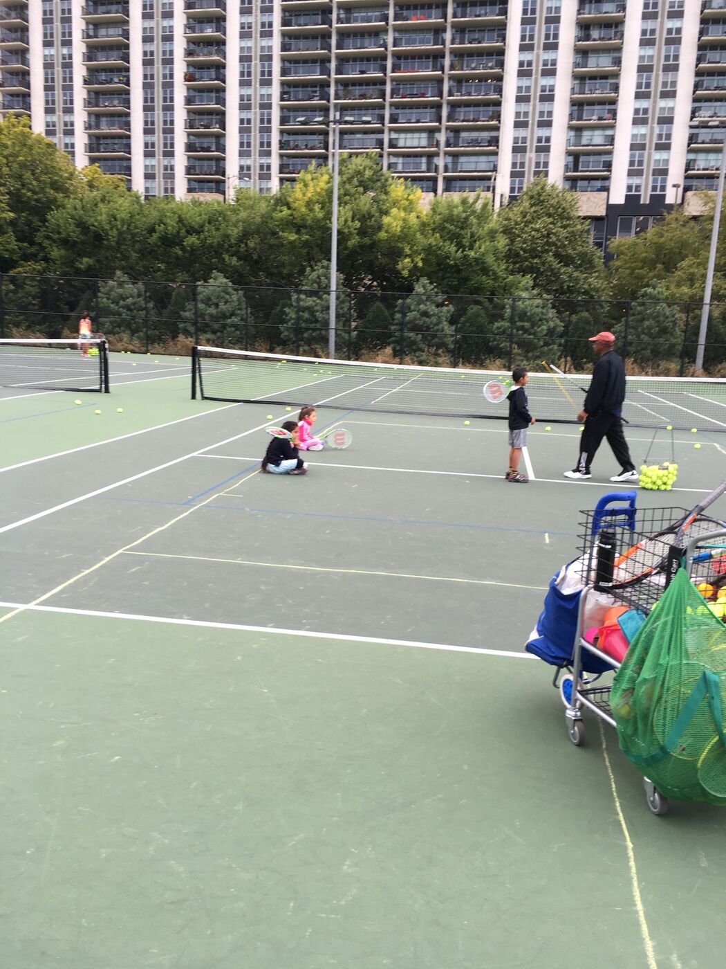 Coach Jay running a group lesson on a city tennis court with young Gabi